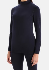 Marinblå långärmad tunneltopp i ett mjukt, stretchigt tyg; åtsittande design med hög krage och minimal logotyp på vänster ärm.