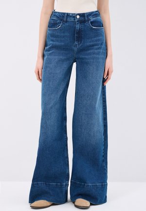 Jeans in denim blu a vita alta con un design a gamba larga, dotati di una chiusura con bottoni, due tasche anteriori e una leggera scoloritura sul tessuto.
