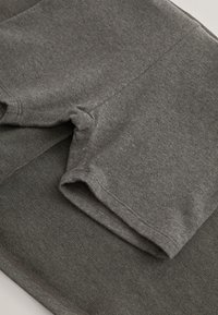 Primo piano di pantaloncini grigi di cotone piegati che mostrano la trama, le cuciture e i dettagli dell'orlo su uno sfondo di tessuto abbinato.