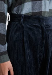 Navy corduroy trousers with a textured finish, featuring a straight fit, subtle pleats, and a waistband with belt loops.