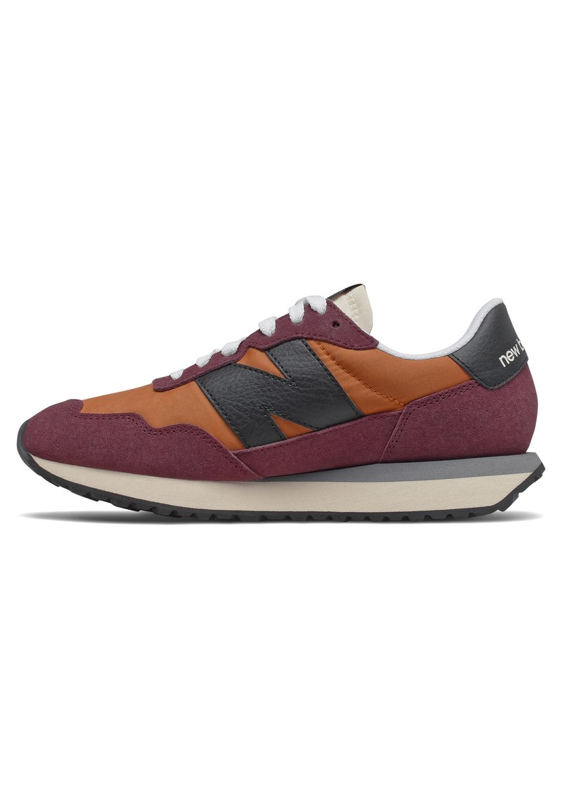 Zapatilla deportiva de ante marrón y naranja con acentos en negro, cordones blancos y suela texturizada. Diseño de perfil bajo con un estilo retro.