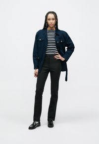 Marineblauw oversized jasje met gouden knopen, gecombineerd met een zwart-wit gestreepte top en strakke zwarte broek, afgewerkt met zwarte loafers.