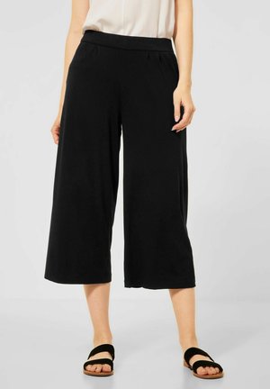 Svarta vida byxor med en slät tyg, elastisk midja och veck. Matchas med svarta platta sandaler.