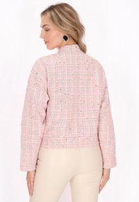 Rosa tweedjakke med en cropped design og lange ærmer. Den strukturerede overflade har flerfarvede prikker og har en høj krave.