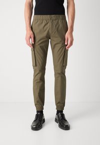 Pantalon cargo vert olive avec taille élastique, deux poches latérales et chevilles ajustées. Fabriqué en tissu léger avec une texture lisse.