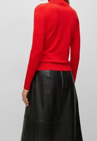 Röd stickad polotröja med långa ärmar, åtsittande midja, matchad med en svart läderkjol med dragkedja och paneldesign.