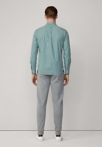 Groen en wit gestreepte langemouwen shirt gecombineerd met grijze joggingbroek, gedragen met witte schoenen met donkerblauwe accenten.