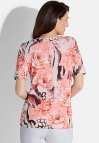 Bloemrijke top met korte mouwen, versierd met grote roze rozen en zwarte accenten op een zachte, gestructureerde stof. De top heeft een ronde halslijn en een relaxed fit.