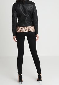 Veste en cuir noir, haut rose à motifs, jean skinny noir et chaussures à talons hauts noires. Vue de dos, mettant en valeur la texture et le design.