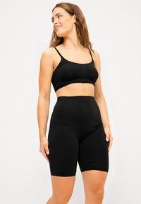 Sort sømløs crop top og høj talje shorts lavet af glat, strækbart stof. Begge items har en tætsiddende pasform og justerbare stropper.