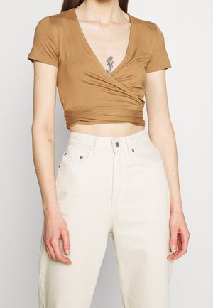 Haut cache-cœur marron à manches courtes en tissu doux, doté d'un décolleté en V profond et d'une coupe ajustée, associé à un pantalon taille haute de couleur crème.