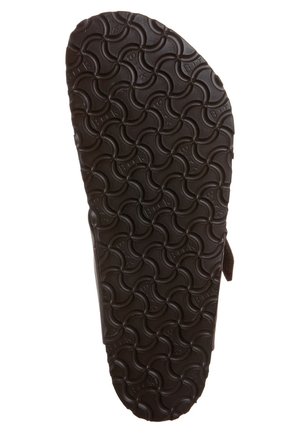 Sole of a brown sandal with a curved, interlocking wave pattern tread and a partial strap visible on the side.