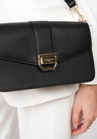 Borse a mano in pelle nera con finitura testurizzata, chiusura in hardware dorato e tracolla removibile. Presenta un design geometrico sulla pattina.