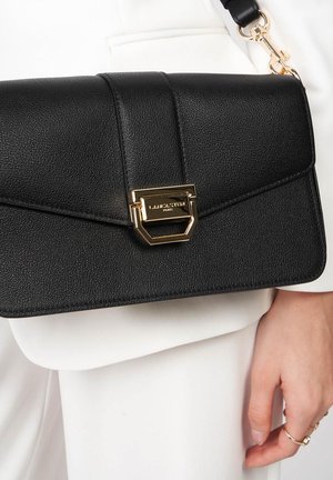 Sac à main en cuir noir avec une finition texturée, fermoir en métal doré et une bandoulière amovible. Présente un design géométrique sur le rabat.