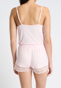 Lichtroze slaapset bestaande uit een mouwloze top en shorts. De shorts hebben een kanten rand aan de zoom en de stof lijkt zacht en glad te zijn.