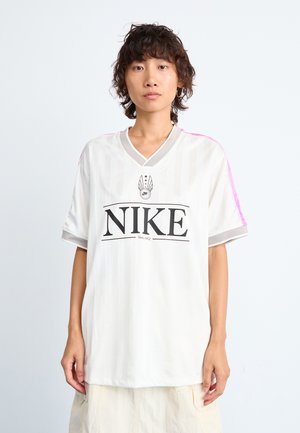 Hvit Nike-drakt med vertikale striper, korte ermer, grå v-hals, og rosa detaljer på skuldrene; har en dristig svart logo i midten.