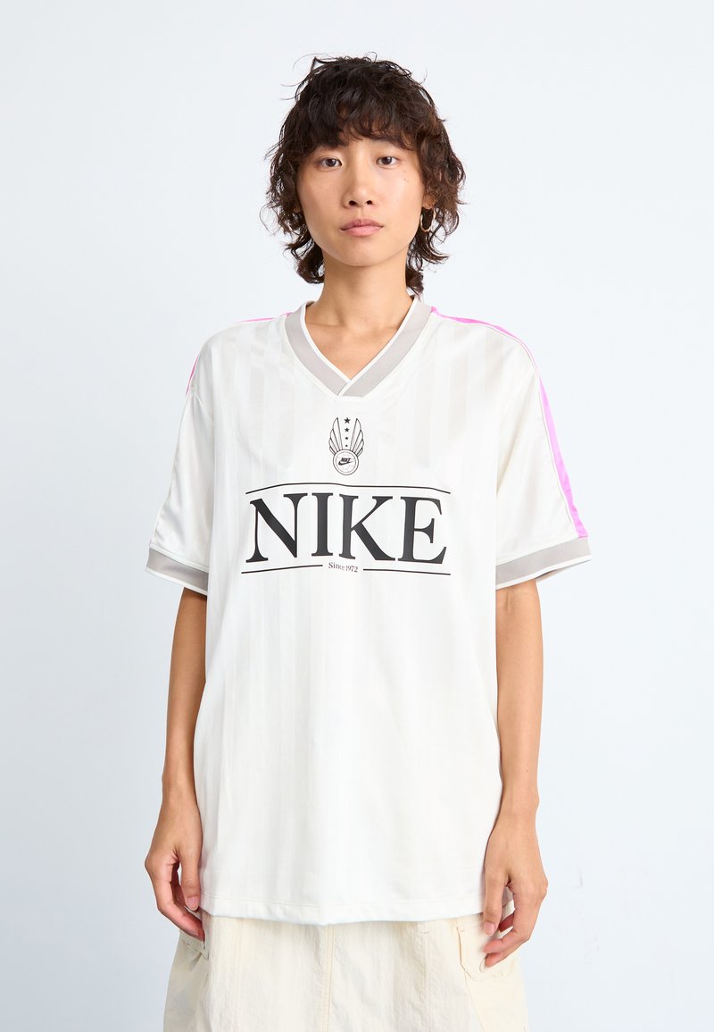 Jersey blanco de Nike con rayas verticales, mangas cortas, cuello en V gris y acentos rosas en los hombros; presenta un logotipo negro en bold en el centro.
