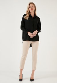 Fekete, hosszú ujjú, gombos ing, egyenes szabással, bézs, slim-fit nadrággal és fekete magassarkú cipővel párosítva. Minimalista dizájn.