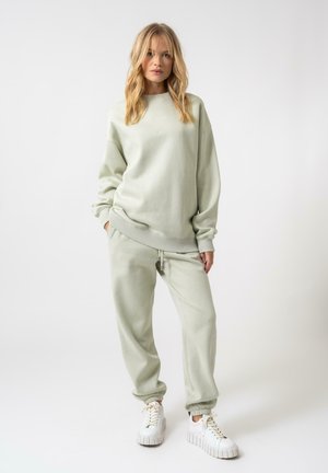 Felpa verde chiaro con polsini e orlo a coste, abbinata a pantaloni jogger coordinati con un cordoncino regolabile. Indossata con sneakers bianche chunky.