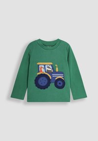 Vihreä pitkähihaine paita, jossa on applikoitu sininen traktori, jonka kanssa on kettu ja mäyrä, korostettuna keltaisella ja mustalla yksityiskohdalla.