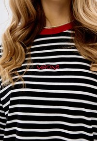 Czarny i biały t-shirt w paski z czerwonym ściągaczem w okolicy szyi oraz haftem "MIRONS" w kolorze czerwonym, charakteryzujący się luźnym krojem i miękką teksturą materiału.
