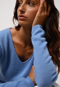 Svetle modrý, měkký svetr s výstřihem do V a dlouhými rukávy. Tkanina vypadá strukturovaně a útulně, s volnějším střihem.
