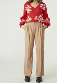 Röd v-ringad tröja med vita blommönster, i kombination med beige plisserade byxor. Svarta plattformsskor. Mjuka texturer och avslappnad passform.