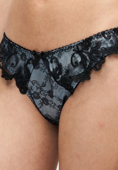 Γυναικεία εσώρουχα από γκρι και μαύρη δαντέλα με λουλουδάτα σχέδια και μικρό μαύρο φιόγκο μπροστά, φορεμένα στους γοφούς και στο επάνω μέρος των μηρών ενός ατόμου.