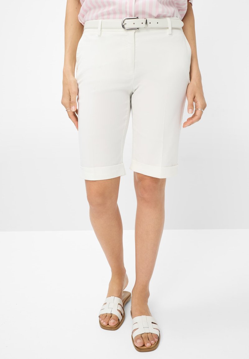 Witte op maat gemaakte bermuda shorts met opgerolde manchetten, een gladde textuur, een bijpassende witte riem, en gedragen met lichtgekleurde instapsandalen.