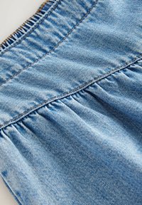 Lichtblauwe denimstof met een geplooide textuur aan de bovenkant, met zichtbare stiksels en een zachte, versleten uitstraling.