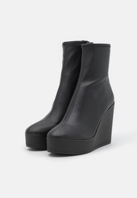 Black leather ankle boots with a wedge heel. Features a smooth surface, round toe, and zipper closure at the back. Textured sole for grip.