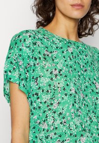 Blusa de tela ligera con un estampado floral verde. Presenta mangas cortas y sueltas, y un escote redondo con un acabado texturizado.