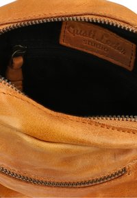 Interno di una borsa in pelle marrone chiaro con fodera nera, dotato di una cerniera e un'etichetta dello studio Gusti Leder. Cuciture e dettagli della trama ben visibili.