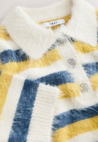 Cardigan en maille duveteuse avec des rayures jaunes, bleues et blanches, des boutons ornés de perles et un col pointu marqué "NEXT."