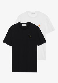 Two cotton t-shirts: one black with a small green and yellow pineapple embroidery, and one white with a circular orange embroidery.