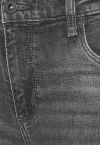 Dark gray denim jeans with a smooth texture, featuring a metal button, stitched detailing, and a classic five-pocket design.