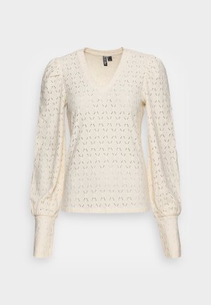 Blouse longue à manches longues en dentelle crème, encolure en V, épaules bouffantes et poignets ajustés avec un délicat motif ajouré répétitif.