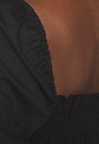 Tessuto nero con un design testurizzato e arricciato, che mette in risalto un collo liscio e una morbida lucentezza sottile. Presenta arricciature elastiche ai bordi.