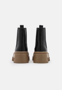 Botas negras de tobillo con un diseño elegante, parte superior de cuero texturizado y suela de goma beige gruesa con tacos pronunciados y tiradores en la parte trasera.