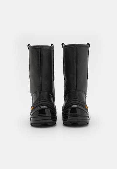 Botas de cuero negro con un acabado texturizado, caña alta, lengüetas en la parte superior y suelas de goma negra brillantes. Diseño duradero para uso al aire libre.