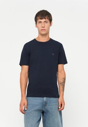 T-shirt en coton bleu marine avec un col rond et des manches courtes, arborant un petit logo brodé sur la poitrine gauche. Ajustement classique.