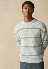 Light gray, ribbed knit sweater with horizontal dark gray stripes. Classic crew neckline and relaxed fit. Paired with blue denim jeans.