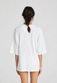 Witte oversized t-shirt met korte mouwen, gekenmerkt door een ronde halslijn en een gladde textuur, weergegeven vanuit de achterkant.