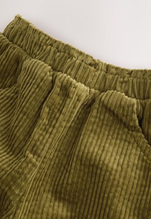 Zelená olivová kordurová látka s žebrovanou texturou a elastickým pasem. Má měkký, plyšový povrch s výraznými vertikálními liniemi.