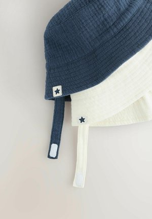 Divkrāsains bucket cepure, kas iezīmē teksturētu tumši zilu augšējo daļu un krēma apakšējo daļu, ar zvaigžņu rotājumiem un kontrastējošām detaļām.