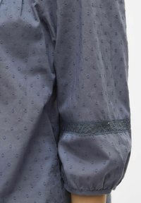 Námořnická modrá, strukturovaná blůza s balónov�ými rukávy, zdobená vyšívanými tečkami a krajkovými detaily na rukávech, vyrobená z lehkého materiálu a s volným střihem.