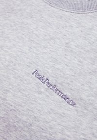 Felpa grigia chiara con finitura testurizzata; presenta un logo blu "PeakPerformance" ricamato verticalmente sul petto.