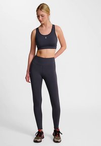 Zwarte sportbeha met een aansluitend ontwerp, gecombineerd met bijpassende hoge taille legging, beide gemaakt van rekbaar materiaal. Draagt sneakers.