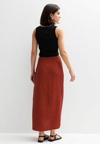 Top senza maniche nero in tessuto ribbed abbinato a una lunga gonna maxi texturizzata color ruggine e sandali neri. Linee semplici e pulite.