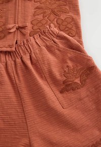 Rustfarvet tekstureret stof med blomsterbroderi på elastikbåndbukser og matchende top med sløjfedetalje.
